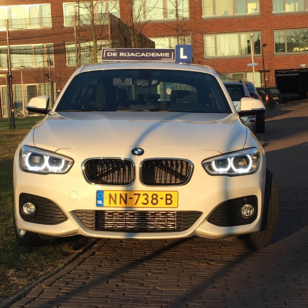 De witte BMW 1-serie lesauto van De Rijacademie met L-bord op het dak